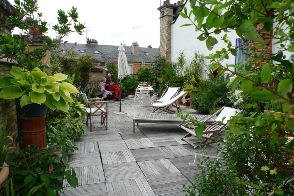 Terrasse de Toit : Jardin Urbain et Détente en Plein Air Terrasse de toit verdoyante avec sol en bois. Un homme et une enfant lisent sur un banc, entourés de plantes et mobilier d'extérieur.