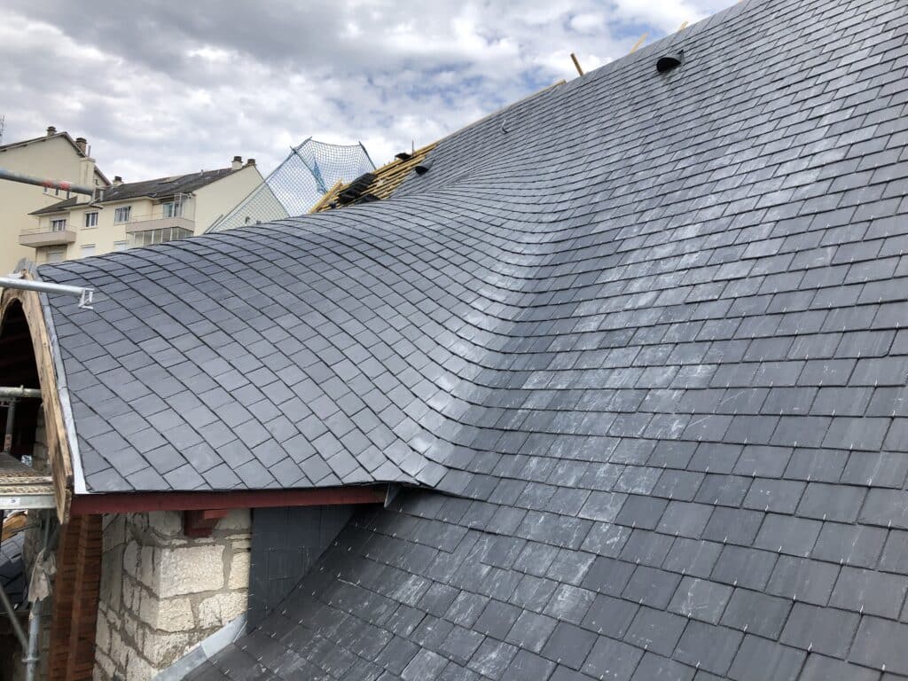 Ardoise Toiture : Rénovation et pose complexe sur toit courbe. Rénovation d'un toit en ardoise sombre. Gros plan sur la pose des tuiles plates sur une surface à double courbure, avec échafaudage et filet de sécurité.