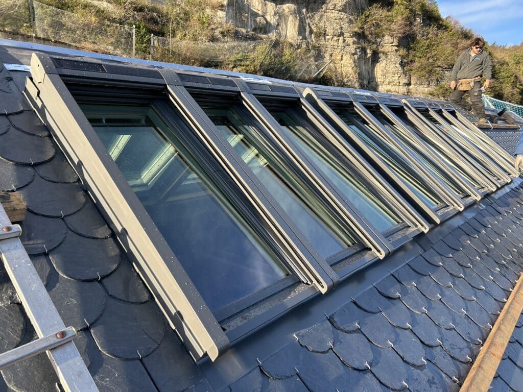 Installation de fenêtres de toit Velux sur toiture ardoise Installation de fenêtres de toit sur une toiture en ardoise par un couvreur professionnel sur un chantier.
