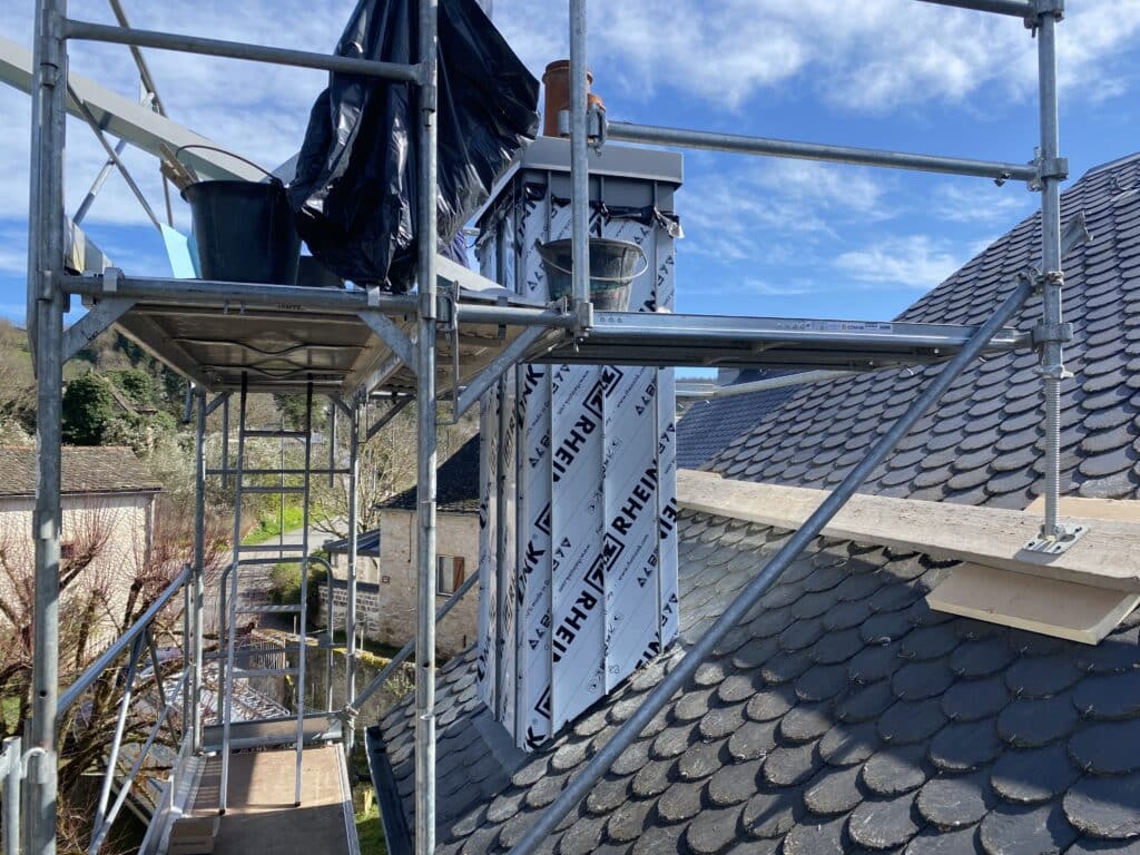 Rénovation de cheminée Rheinzink sur toit en ardoise Échafaudage autour d'une cheminée en rénovation recouverte de film RHEINZINK sur un toit en ardoise.