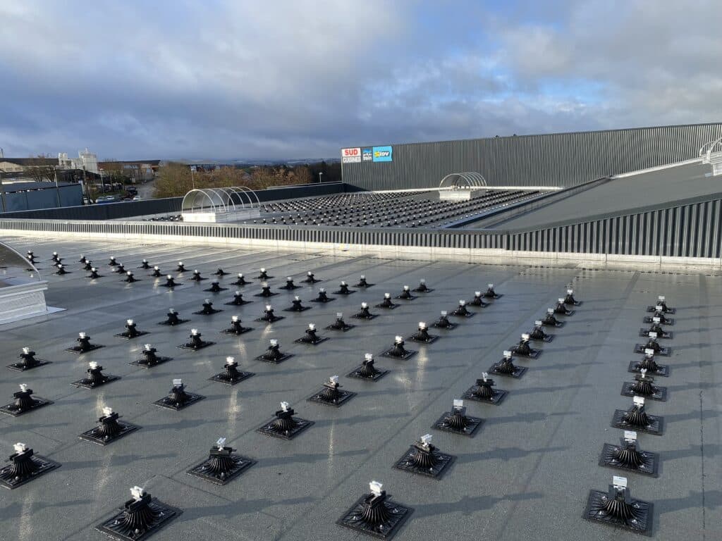 Supports de fixation pour toiture SUD CUISINES SIDV Toit industriel avec plots de support et lanterneaux, enseignes SUD CUISINES et SIDV visibles sous ciel nuageux.